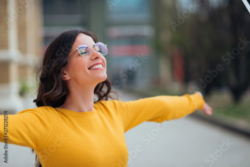 Young woman with toothy smile and eyes closed spreading arms wide open, in the city.