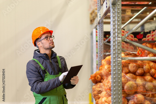 Young warehouse worker looking at shelves with vegetables. photo