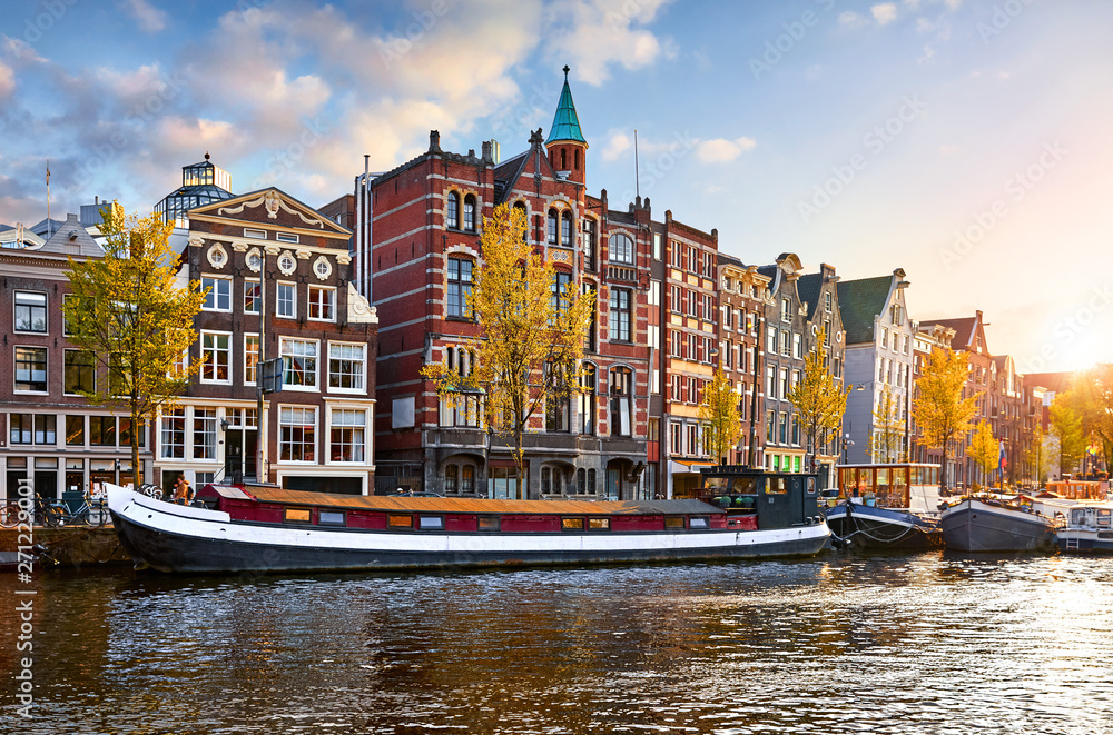 Obraz premium Amsterdam, Netherlands. Floating Houses and houseboats and boats at channels by banks. Traditional dutch dancing houses among trees. Evening autumn street above water pink sunset sky with clouds.
