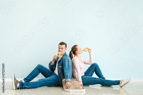 Young couple eating tasty pizza near light wall
