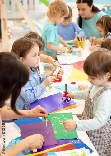 Development learning children in preschool. Children s project in kindergarten. Group of kids and teacher cutting paper and gluing with glue stick on art class in kindergarten or daycare