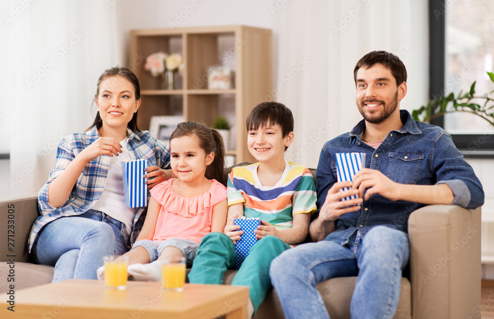 family, leisure and people concept - happy mother, father, son and daughter with popcorn watching tv at home