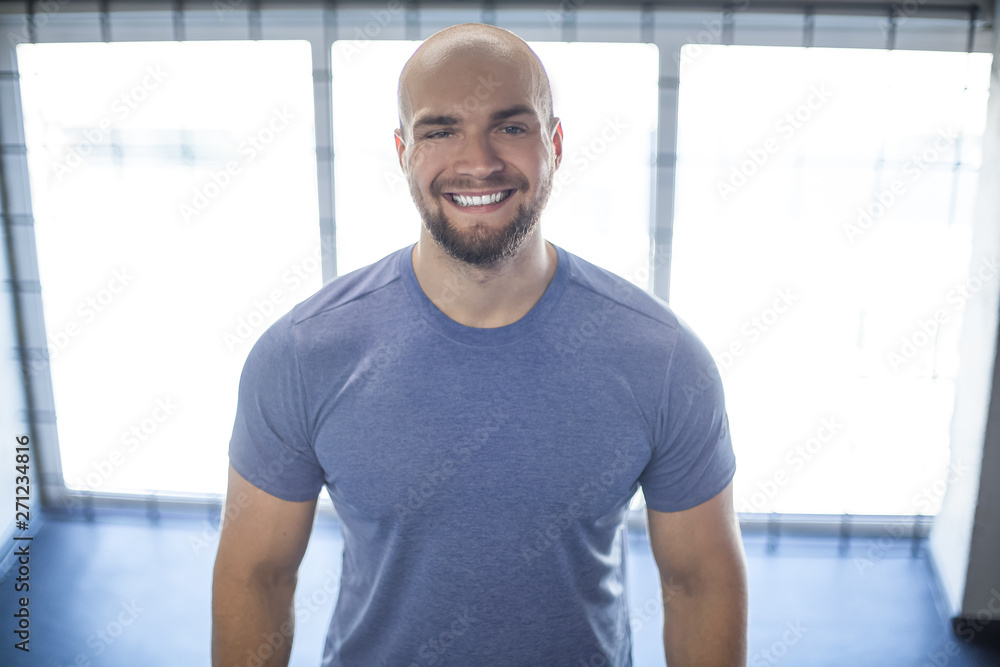 Portrait of a young smiling athlete in the gym. stands on the background of beautiful windows. workout was successful Portrait of a young smiling athlete in the gym. stands on the background of beautiful windows. workout was successful
