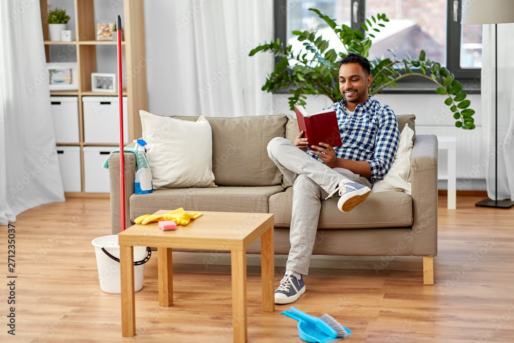 household and people concept - indian man reading book and resting after home cleaning