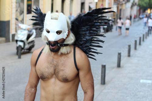 Man wearing dark wings, dog mask and gag ball outdoors 