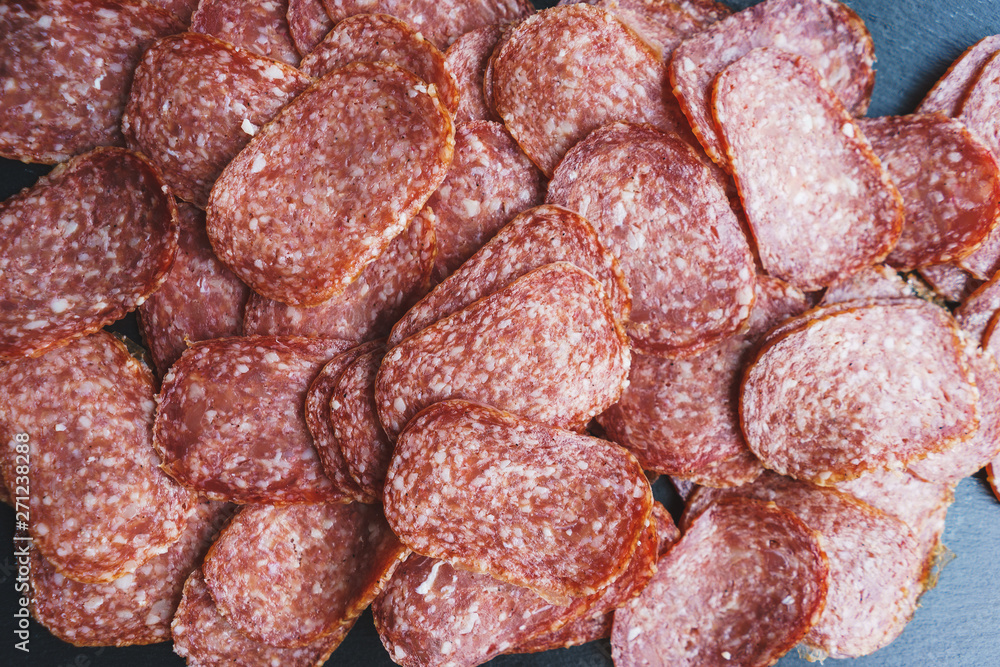Obraz premium Thinly sliced sausage slices on a black stone board. 
