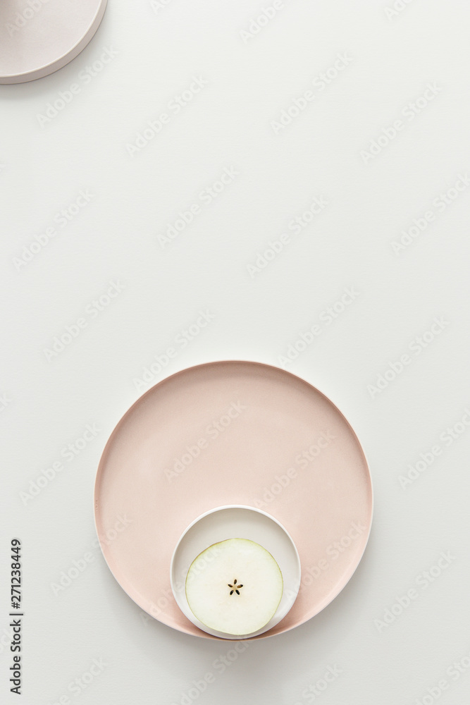 A fresh pear cut in half showing the seeds layed out on a set of pastel powdery rose plates on a light grey table. A fresh pear cut in half showing the seeds layed out on a set of pastel powdery rose plates on a light grey table.