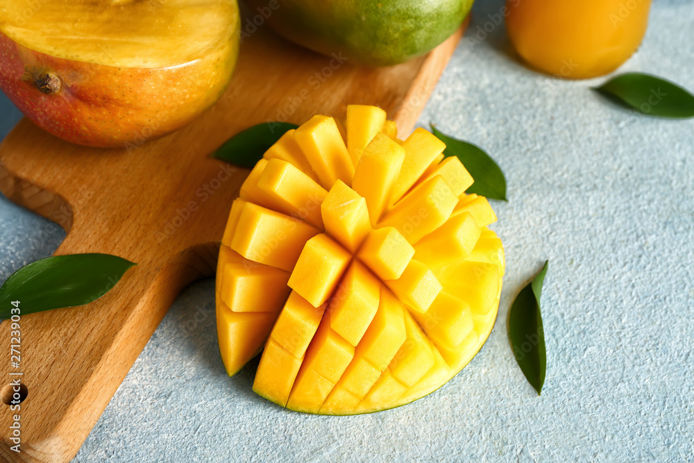 Tasty fresh mango with board on color background