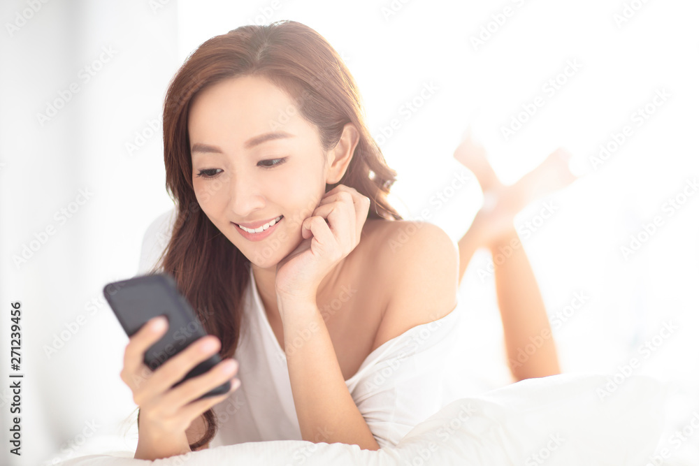 young smiling woman watching mobile phone on bed young smiling woman watching mobile phone on bed
