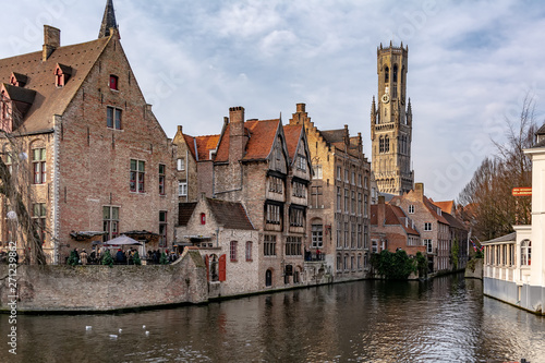 Bruges, Belgium - December 15, 2018: The Rozenhoedkaai (Quay of the Rosary) canal in Bruges with the classic medieval buildings and Belfry of Bruges in the background. Quay of Rosary in sunny day.