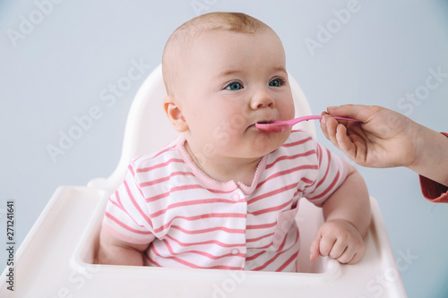 Cute little baby eating tasty food on grey background