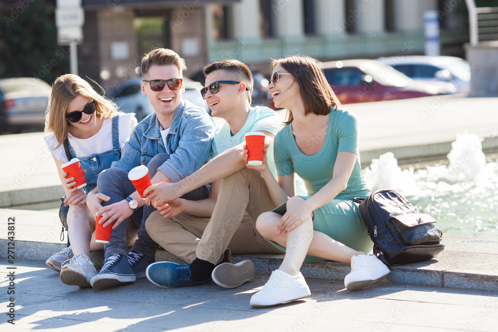 Fototapeta premium Young attractive people having fun together outdoors. People drinking coffee and smiling. Group of friends walking together.