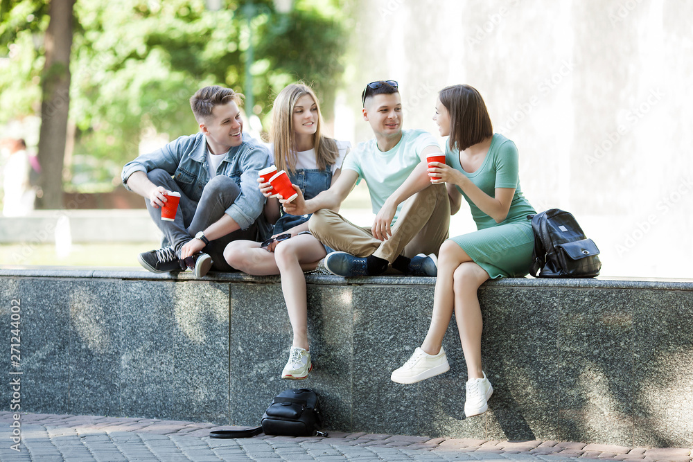 Fototapeta premium Young attractive people having fun together outdoors. People drinking coffee and smiling. Group of friends walking together.