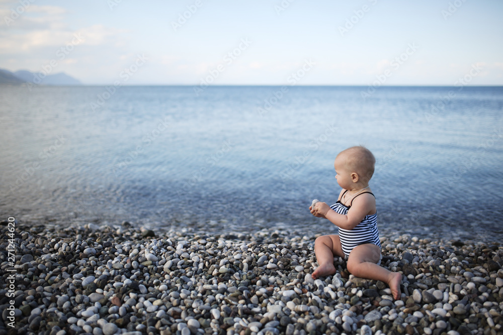 baby in a striped swimsuit by sea on pebble area