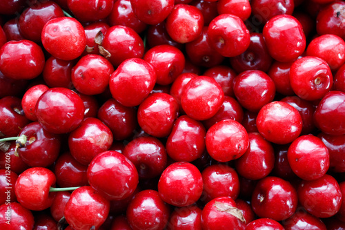 Close up of a pile of ripe cherries with stalks and leaves. A large collection of fresh red cherries. Ripe cherry background. Close-up.