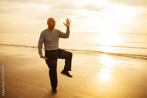 Asian Senior old man practice Tai chi and Yoga pose on the beach sunrise