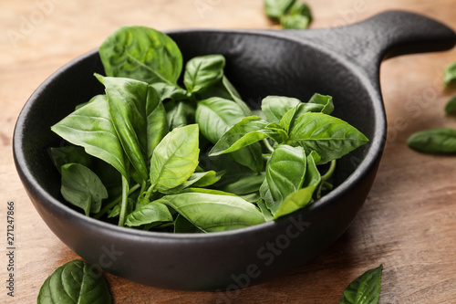 Frying pan with fresh basil leaves on wooden background