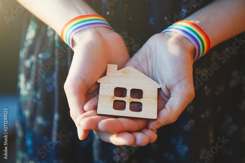 young female hands with LGBT rainbow ribbon wristbands holding craft wooden house