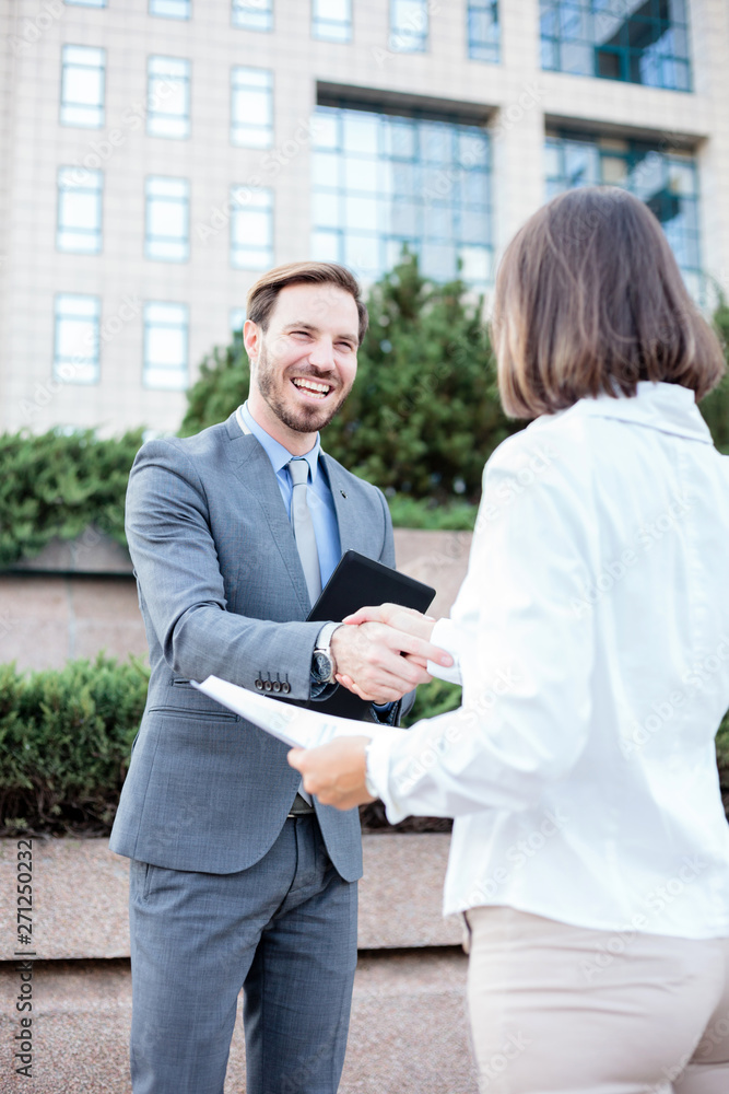 Young female and male businesspeople shaking hands after a successful meeting in front of an office building. Low angle view. Working in urban city streets Young female and male businesspeople shaking hands after a successful meeting in front of an office building. Low angle view. Working in urban city streets