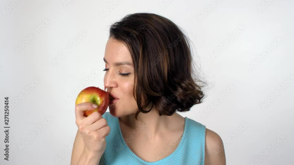 Portrait of beautiful young woman standing isolated on white background and biting tasty red apple, then chewing and looking at camera Portrait of beautiful young woman standing isolated on white background and biting tasty red apple, then chewing and looking at camera