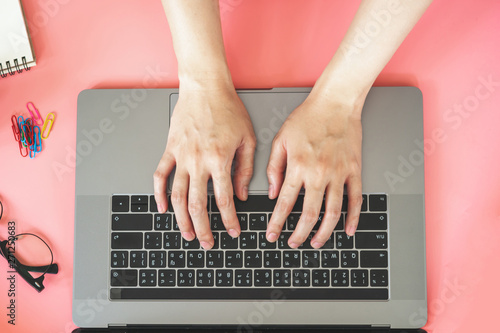 Women typing on laptop in pink pastel colourful office with accessories