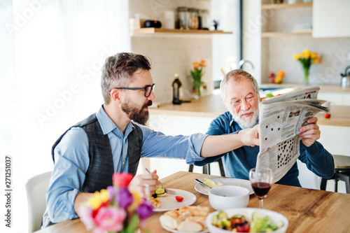 An adult hipster son and senior father indoors at home  eating light lunch.