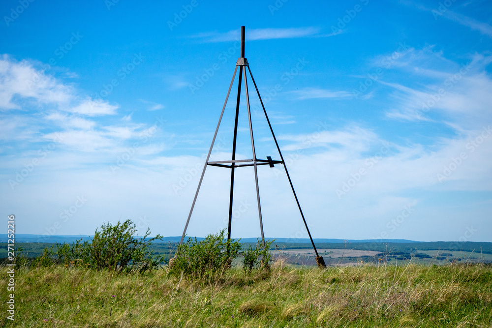 Metal tower on top of a hill. Geodesic, triangulation point. Summer landscape.
