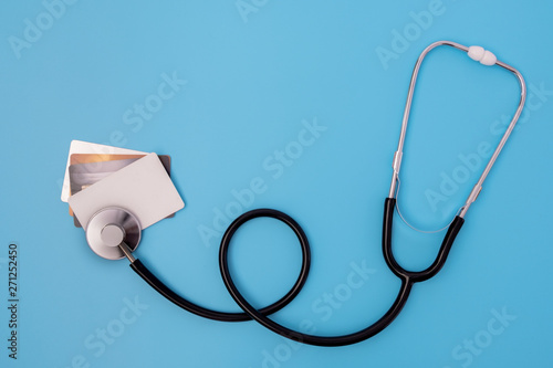 Flat lay black stethoscope checking financial limit of four credit card for expense of medical care cost and health insurance concept on blue background