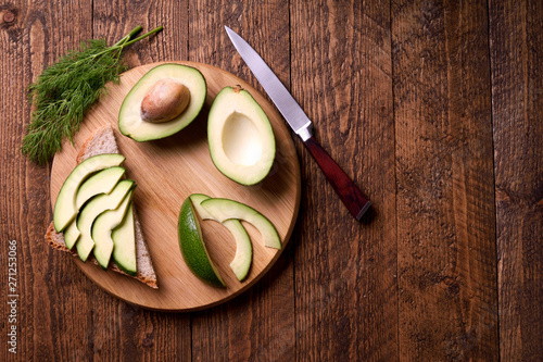 Beautifully plated avocado toast with delicious-looking toppings on wooden brouw background. Making sandwiches with avocado healthy organic food top view.On A Wooden Cutting Board Sliced avocado. photo
