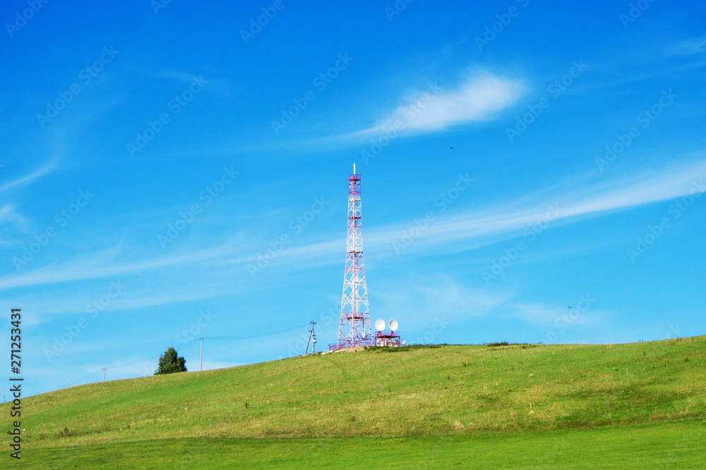Summer landscape. Tower of mobile communications on a hill against the blue sky.