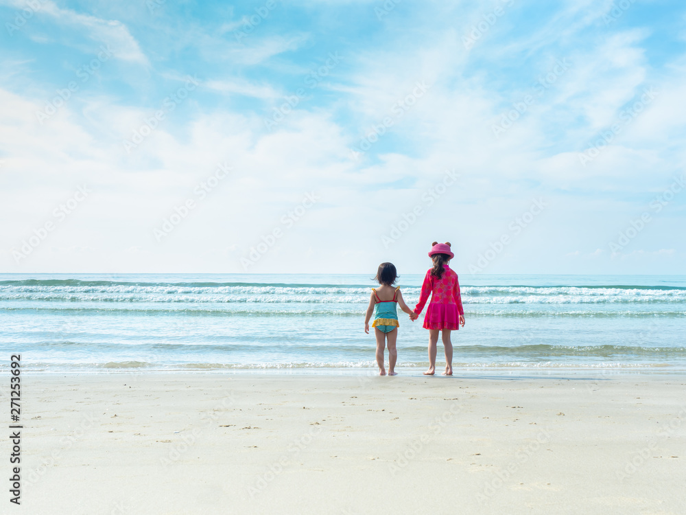 Two little girls are standing and hand to hand at the beach and sea. Older sister holding hand younger sister to play at the beach and sea.