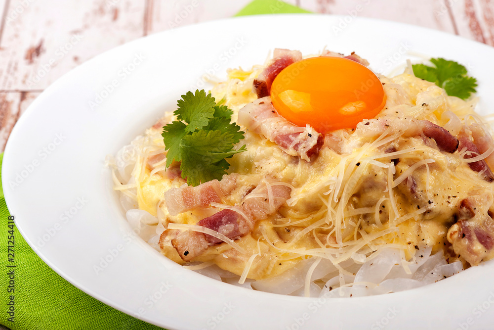 Traditional dish of Italian cuisine carbonara sauce with low-carb shirataka paste and egg yolk. Large portion served on a white plate. Close up and horizontal view. Traditional dish of Italian cuisine carbonara sauce with low-carb shirataka paste and egg yolk. Large portion served on a white plate. Close up and horizontal view.