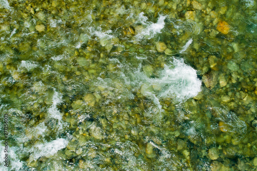 Top view of mountain river water with rocks and splashes. Background of fresh water with fast rapids in alpine river.