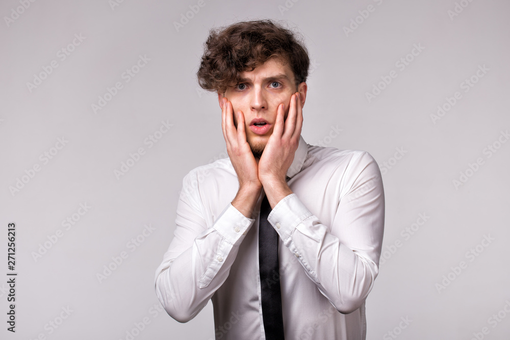 Portrait of young man with shocked emotional facial expression and hands gesture over light gray background