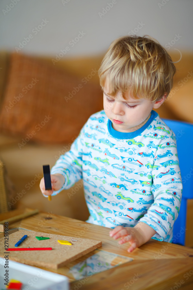 Cute toddler boy playing with wooden hammer tool at home in workshop. Kid boy play as handyman. Child in night clothes playing as builder or repairer, repairing or handcrafting. Handcrafting concept. Cute toddler boy playing with wooden hammer tool at home in workshop. Kid boy play as handyman. Child in night clothes playing as builder or repairer, repairing or handcrafting. Handcrafting concept.