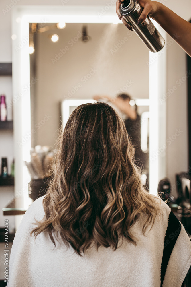 Beautiful young woman with long curly hair in hair salon. Professional  hairdresser styling with hairspray. Stock Photo | Adobe Stock