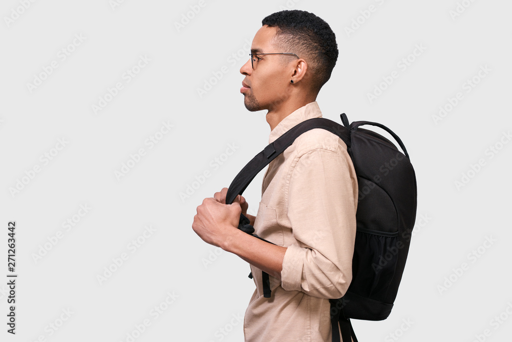 Side view image of young Afro man student with backpack standing over white  wall. Young businessman