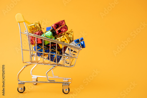 Christmas gifts in a supermarket trolley on yellow background. Online shopping concept - trolley full of gifts. Black Friday and Cyber Monday
