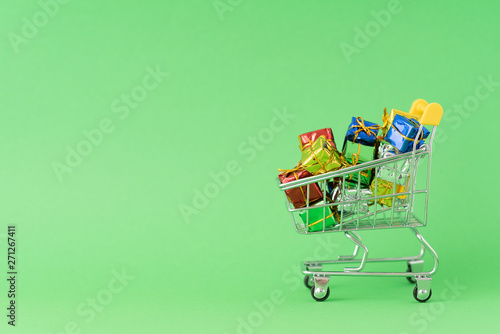 Christmas gifts in supermarket trolley on green background. Online shopping concept - trolley full of gifts. Black Friday and Cyber Monday