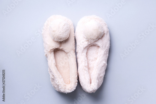Nude fluffy home slippers with pompon on pastel grey background. Top view. Copy space. Cozy home footwear. Sweet home and spa, body treatment concept