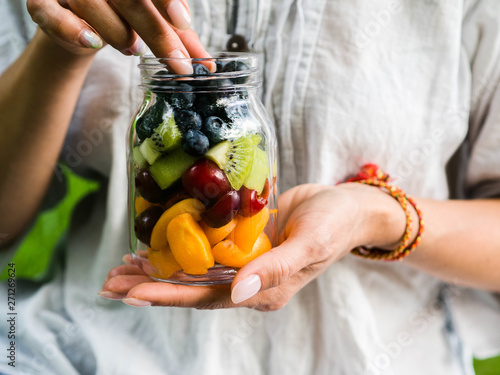 Foto A glass jar with a salad of fruits and berries in the hands of a woman