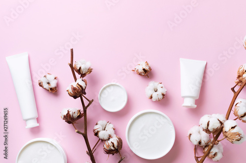 Fluffy cotton flowers, face cream, body butter on pink background with copy space. Cosmetics, beauty, spa concept. Top view. Flat lay