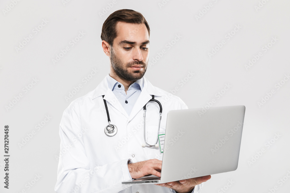 Portrait of caucasian young medical doctor with stethoscope working in clinic and holding laptop