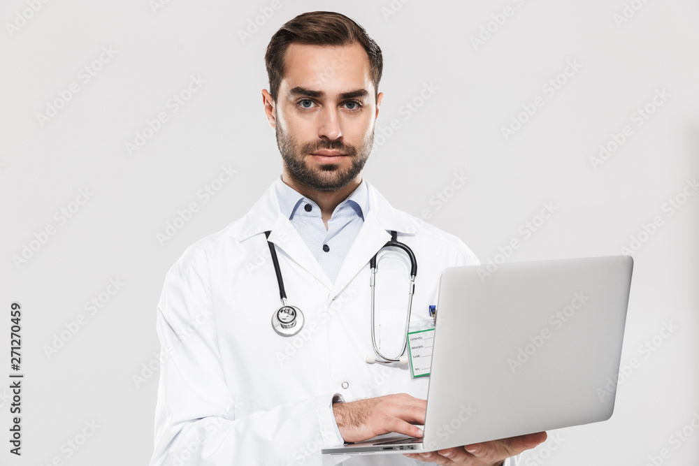 Portrait of smart young medical doctor with stethoscope working in clinic and holding laptop Portrait of smart young medical doctor with stethoscope working in clinic and holding laptop