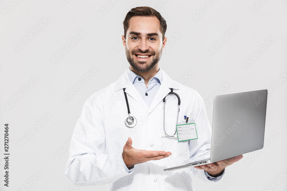 Portrait of handsome young medical doctor with stethoscope working in clinic and holding laptop Portrait of handsome young medical doctor with stethoscope working in clinic and holding laptop