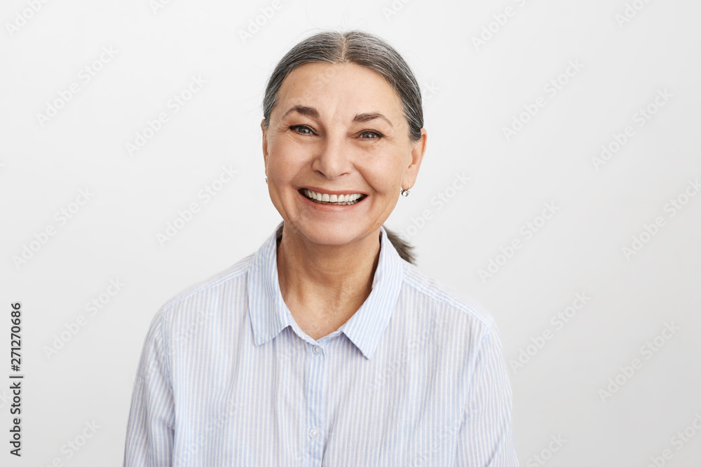 Joy, happiness, aging, old people and positive vibrations concept. Picture of happy elegant senior 65 year old female in good mood wearing blue shirt looking at camera with broad cheerful smile Joy, happiness, aging, old people and positive vibrations concept. Picture of happy elegant senior 65 year old female in good mood wearing blue shirt looking at camera with broad cheerful smile