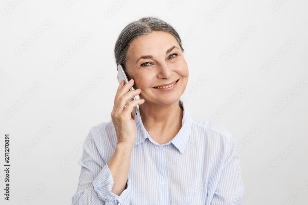 Joyful attractive elderly gray haired female in her sixties rejoycing at good news, smiling broadly while talking on mobile phone to her daughter. People, communication, gadgets and modern technology Joyful attractive elderly gray haired female in her sixties rejoycing at good news, smiling broadly while talking on mobile phone to her daughter. People, communication, gadgets and modern technology