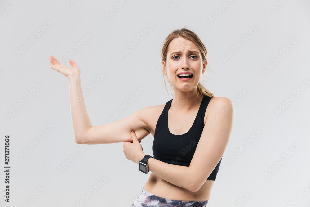 Image of disappointed blond woman 20s dressed in sportswear crying while touching her fat arm during workout in gym is Image of disappointed blond woman 20s dressed in sportswear crying while touching her fat arm during workout in gym is