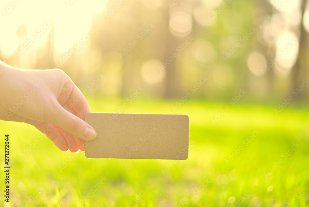 Hand holding empty card in a park in sunny rays.  Background. Copy space.