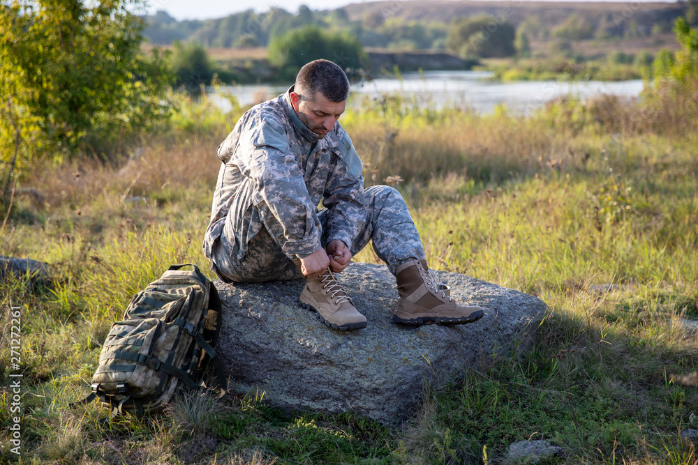 Soldier tying shoes. Soldier. Soldier in gear. The soldier sits and rests.	
